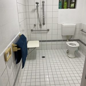 spacious white tiled accessible bathroom with toilet, shower and grab rails