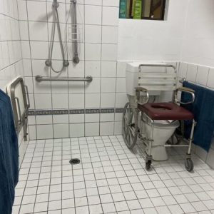 Tiled accessible motel room bathroom with wheelchair seat over toilet